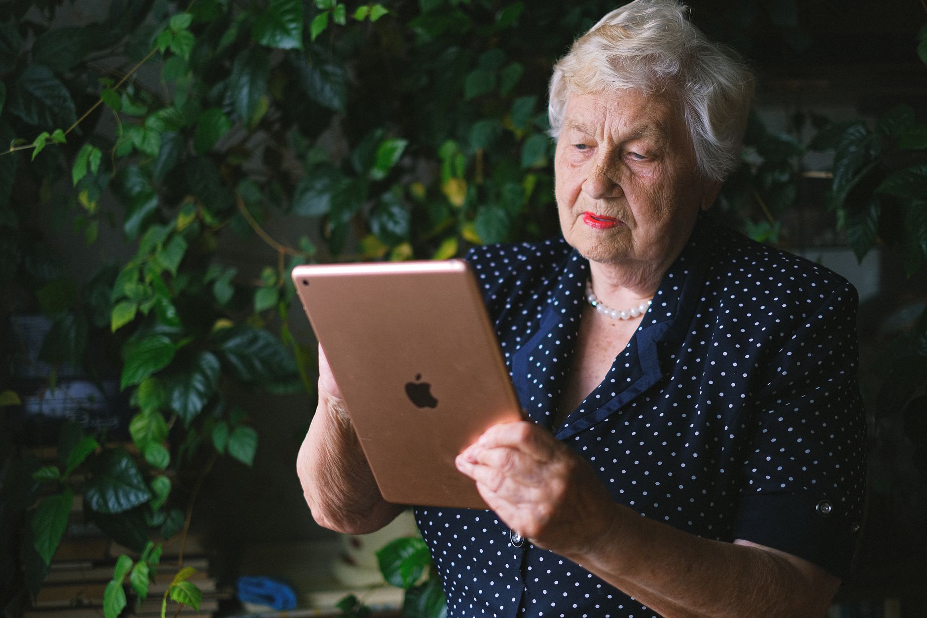 Woman with short white hair looking at a rose-gold tablet in front of green foliage
